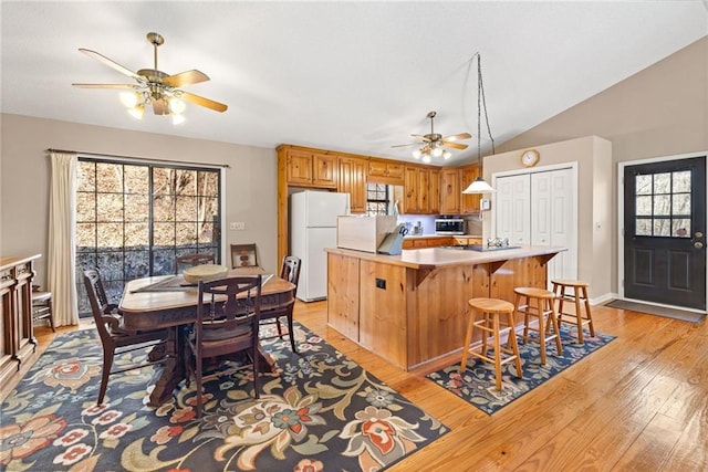 kitchen with light countertops, stainless steel microwave, freestanding refrigerator, and light wood-style floors