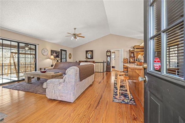 living area featuring lofted ceiling, light wood-type flooring, ceiling fan, and a textured ceiling