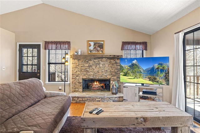 living room featuring a wealth of natural light, vaulted ceiling, and a stone fireplace