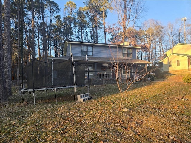 rear view of property featuring a yard and a trampoline