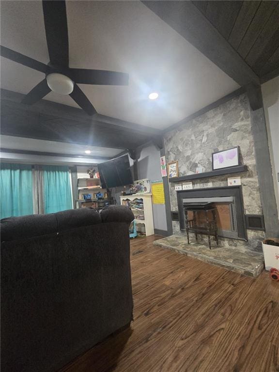 living room featuring beamed ceiling, ceiling fan, wood-type flooring, and a stone fireplace