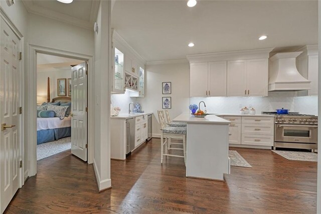 kitchen with custom exhaust hood, white cabinetry, a kitchen bar, stainless steel appliances, and dark hardwood / wood-style flooring