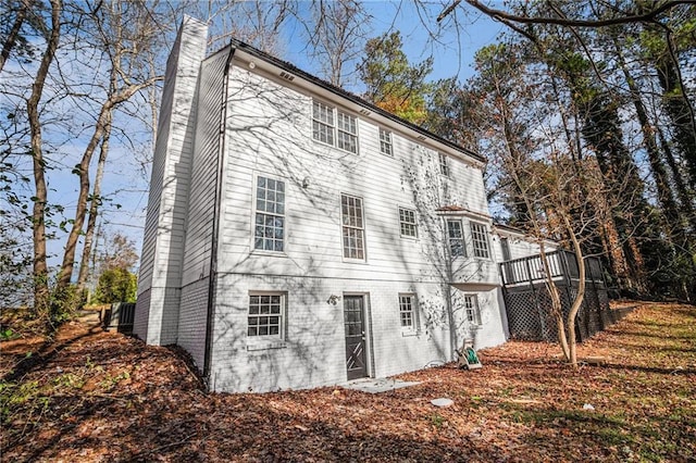 rear view of property featuring brick siding, a chimney, and a wooden deck