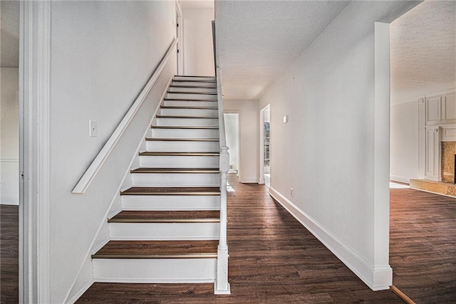 staircase with a textured ceiling, wood finished floors, a high end fireplace, and baseboards