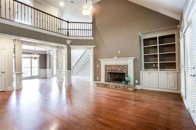 240 Chandler Walk, Loganville, GA 30052 - unfurnished living room with high vaulted ceiling, ornate columns, a brick fireplace, wood finished floors, and a chandelier