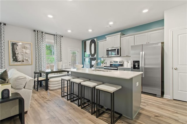 kitchen featuring white cabinets, appliances with stainless steel finishes, a breakfast bar, and an island with sink