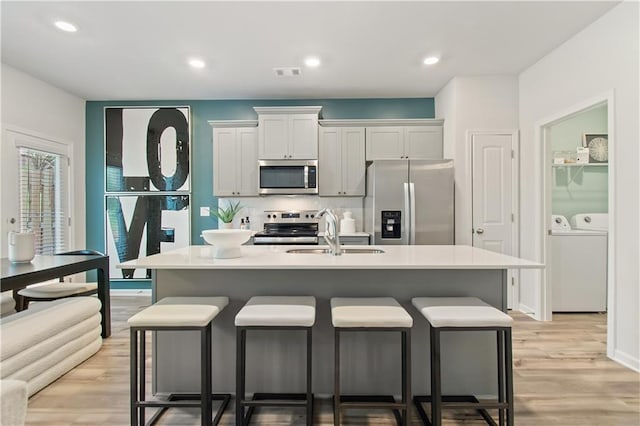 kitchen with a kitchen bar, an island with sink, white cabinets, and stainless steel appliances