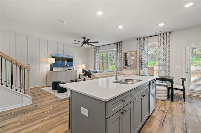 kitchen featuring gray cabinetry, sink, light hardwood / wood-style flooring, stainless steel dishwasher, and an island with sink