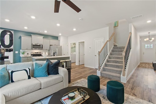 living room with ceiling fan with notable chandelier, washer / dryer, sink, and light hardwood / wood-style flooring