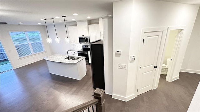 kitchen with appliances with stainless steel finishes, decorative light fixtures, white cabinetry, an island with sink, and sink