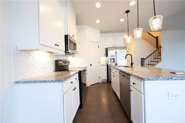 kitchen featuring appliances with stainless steel finishes, white cabinets, hanging light fixtures, light stone counters, and a center island with sink