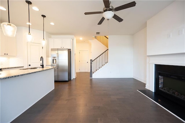 kitchen featuring stainless steel fridge, hanging light fixtures, dark hardwood / wood-style floors, light stone counters, and white cabinets