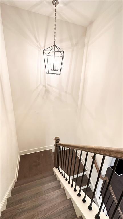 stairway with hardwood / wood-style floors and a notable chandelier