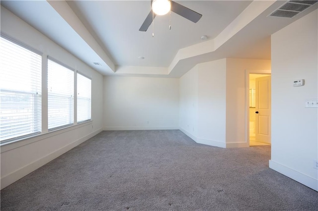 empty room with ceiling fan, carpet flooring, and a tray ceiling