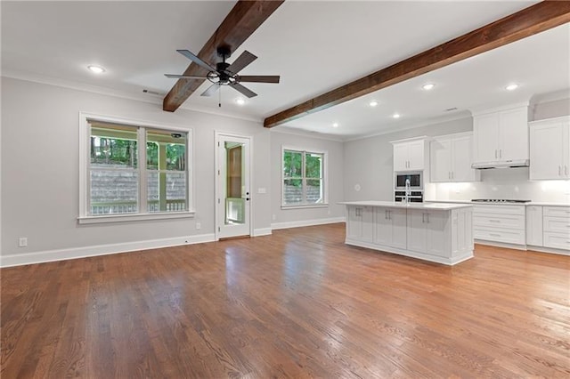 kitchen with a center island with sink, light hardwood / wood-style floors, beam ceiling, and white cabinets