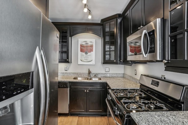 kitchen with rail lighting, sink, light stone counters, appliances with stainless steel finishes, and light hardwood / wood-style floors