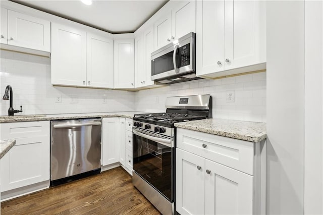 kitchen featuring white cabinets, light stone counters, dark wood-type flooring, stainless steel appliances, and a sink