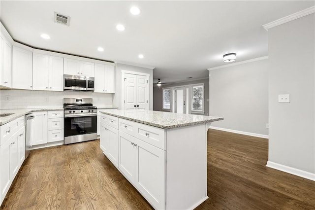 kitchen with light stone counters, a kitchen island, visible vents, white cabinetry, and appliances with stainless steel finishes