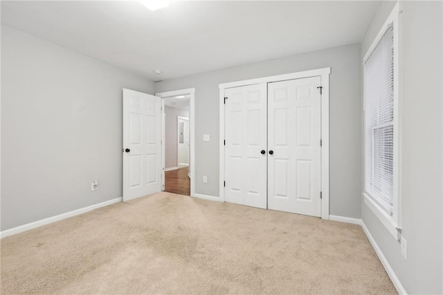 unfurnished bedroom with a closet, light carpet, and baseboards