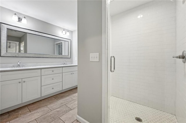 full bathroom with double vanity, wood tiled floor, a sink, and a shower stall