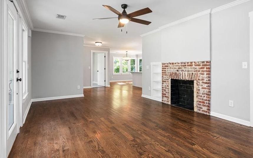 unfurnished living room featuring built in shelves, crown molding, dark wood-type flooring, and a brick fireplace