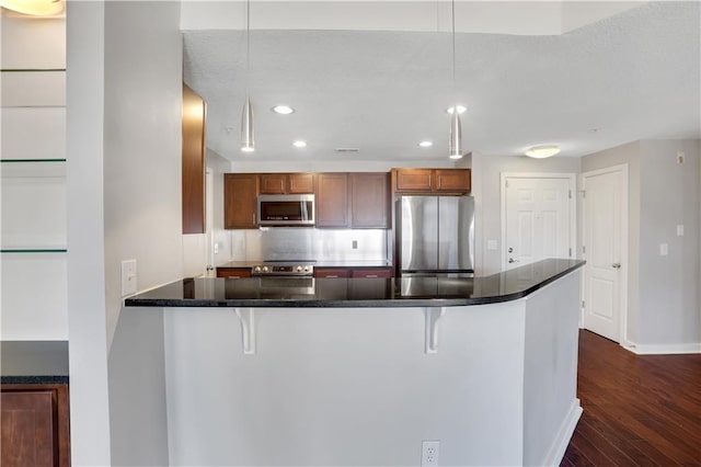 kitchen featuring hanging light fixtures, dark wood-type flooring, a breakfast bar area, and appliances with stainless steel finishes