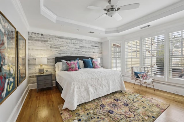 bedroom with wood-type flooring, ceiling fan, crown molding, and a tray ceiling