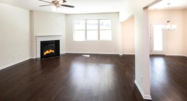 unfurnished living room featuring ceiling fan with notable chandelier and dark wood-type flooring