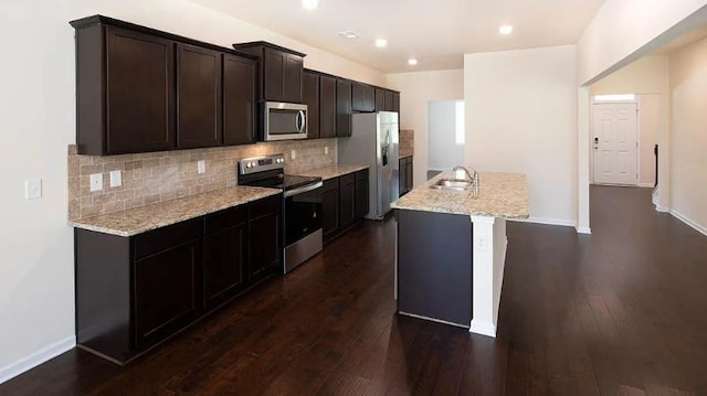 kitchen featuring appliances with stainless steel finishes, light stone countertops, an island with sink, and backsplash