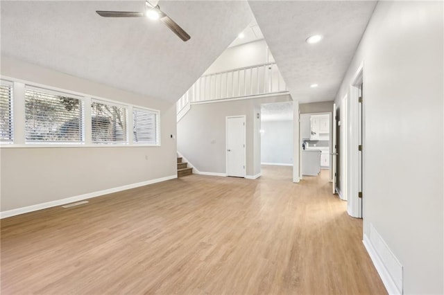 unfurnished living room with ceiling fan, a high ceiling, and light wood-type flooring