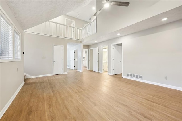 unfurnished living room featuring a towering ceiling, light hardwood / wood-style floors, and ceiling fan