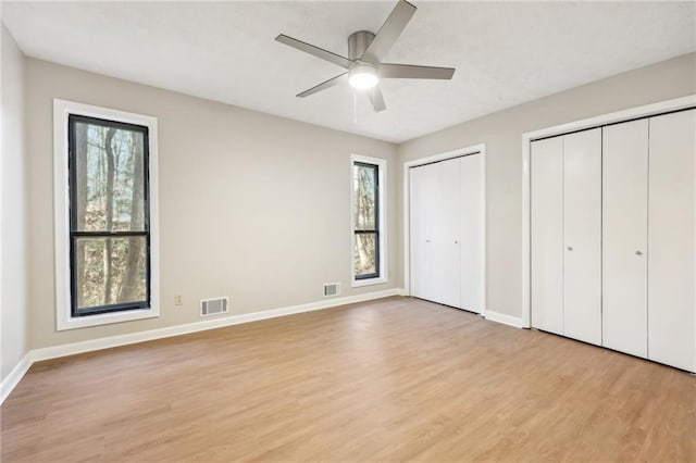 unfurnished bedroom with ceiling fan, light hardwood / wood-style floors, and two closets