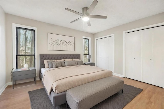 bedroom with two closets, light hardwood / wood-style floors, and ceiling fan