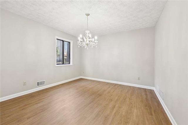 empty room with an inviting chandelier, hardwood / wood-style floors, and a textured ceiling