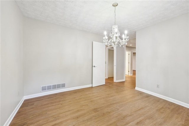 empty room with hardwood / wood-style floors, a textured ceiling, and a notable chandelier