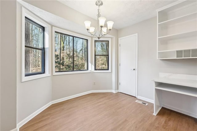 unfurnished dining area featuring wood-type flooring, a wealth of natural light, and a notable chandelier