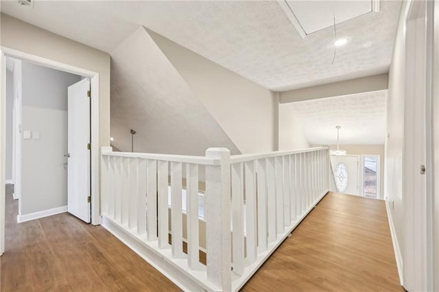 hall with hardwood / wood-style flooring, lofted ceiling, and a textured ceiling