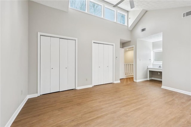 unfurnished bedroom featuring multiple closets, ceiling fan, light hardwood / wood-style floors, and a towering ceiling