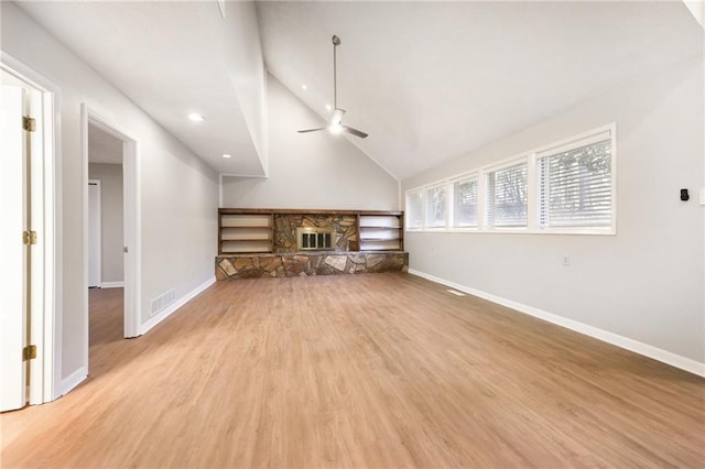 unfurnished living room with ceiling fan, high vaulted ceiling, a stone fireplace, and light hardwood / wood-style floors