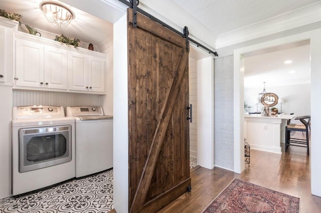 laundry area with a barn door, washing machine and clothes dryer, cabinet space, and wood finished floors