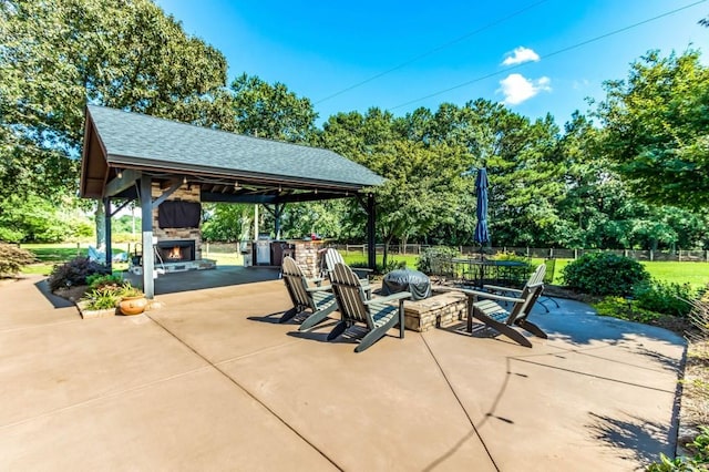 view of patio / terrace featuring an outdoor stone fireplace, view of wooded area, and a gazebo