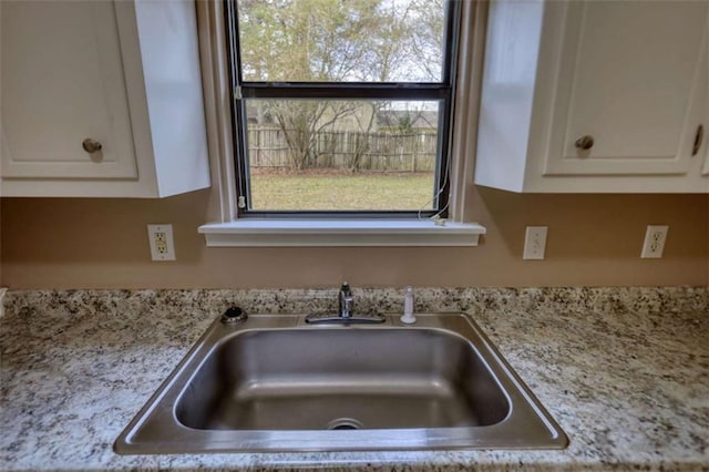 room details with white cabinets, a sink, and light stone countertops