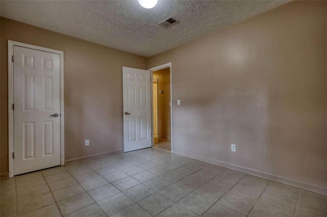 empty room with light tile patterned floors, a textured ceiling, visible vents, and baseboards