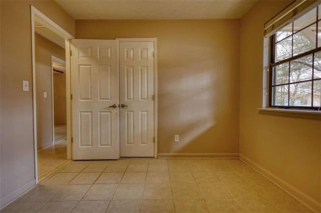 unfurnished bedroom with a textured ceiling, baseboards, and light tile patterned floors