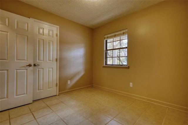 spare room with light tile patterned flooring, a textured ceiling, and baseboards