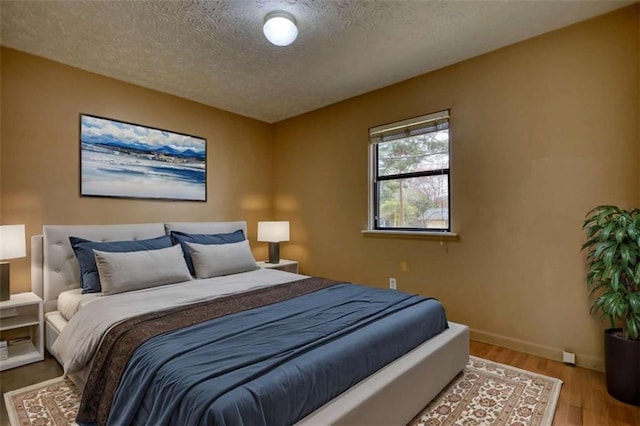 bedroom with a textured ceiling, baseboards, and wood finished floors