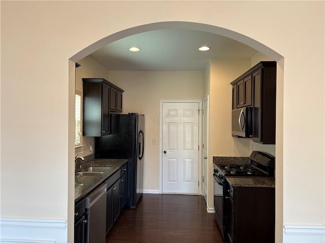 kitchen with dark brown cabinetry, sink, dark hardwood / wood-style floors, dark stone counters, and black appliances