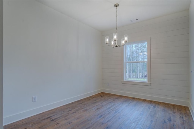 empty room featuring a chandelier, visible vents, baseboards, and wood finished floors