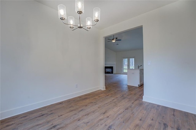 unfurnished room with baseboards, lofted ceiling, wood finished floors, a fireplace, and ceiling fan with notable chandelier