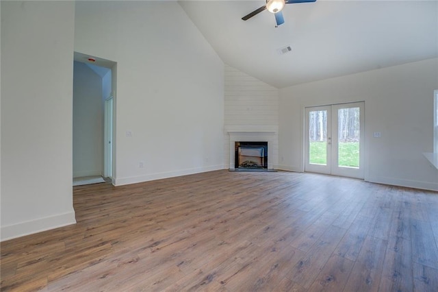 unfurnished living room with high vaulted ceiling, a large fireplace, wood finished floors, visible vents, and baseboards